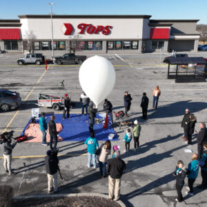 Behind the scenes of a commercial shoot. Crew around an inflated weather balloon in front of Tops store.