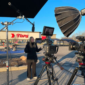 Behind the scenes of a commercial shoot. Woman speaking to cameras in front of a Tops store.