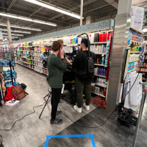 Behind the scenes of a commercial shoot. Crew discussing next scene in an aisle of the store.