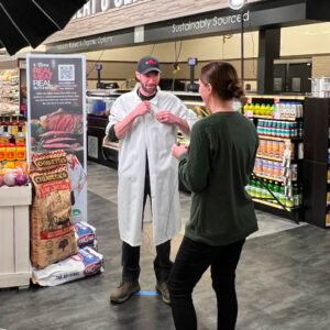 Behind the scenes of a commercial shoot. Art Director helping to microphone a butcher before filming.