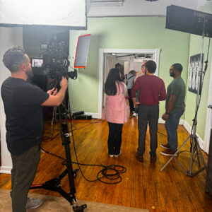 Behind the scenes of a commercial shoot. Cameraman filming actors in a kitchen entryway.