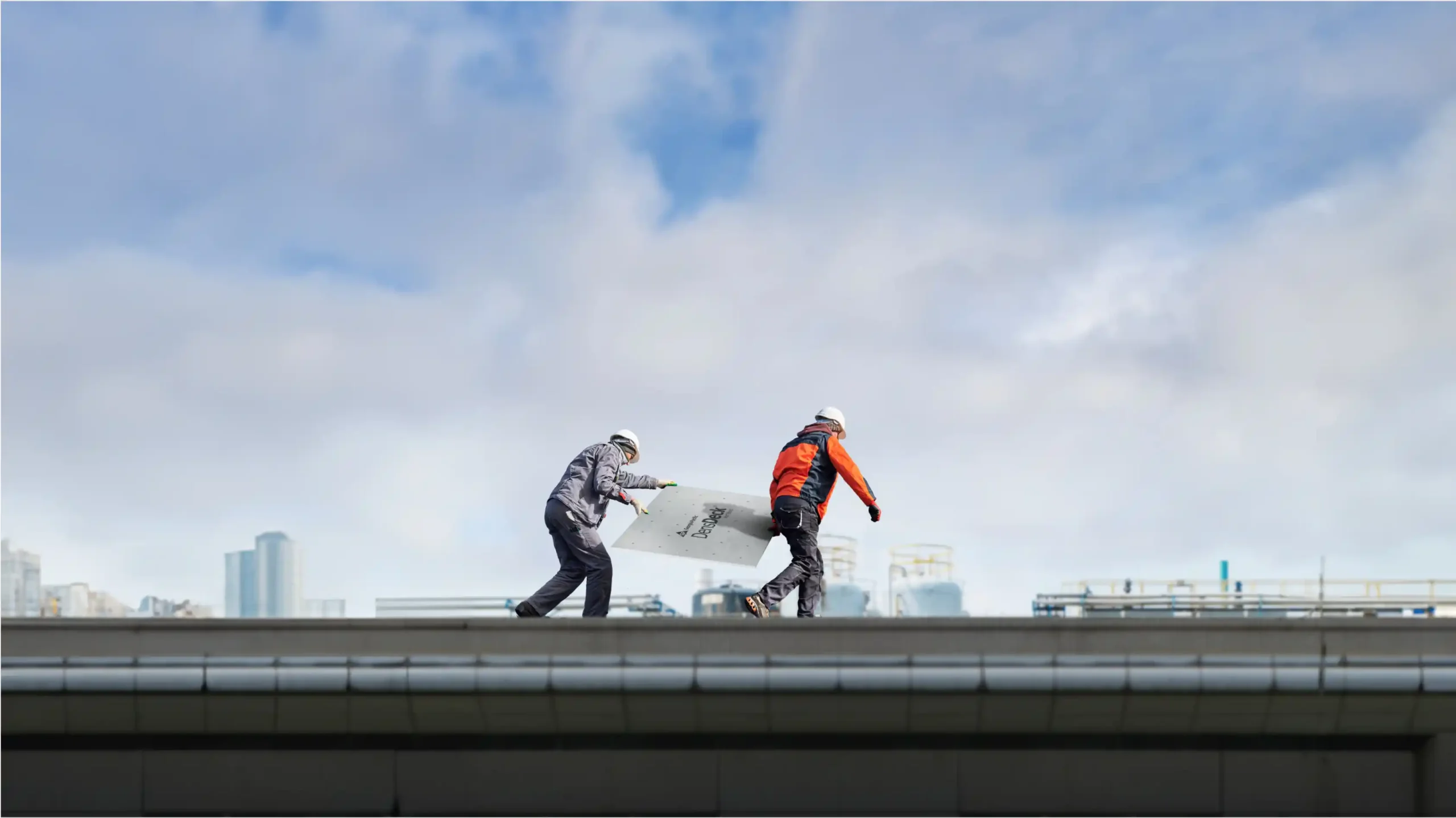 Workers carrying a piece of roofboard on top of an industrial building rooftop