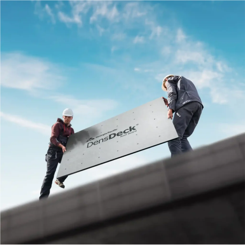 Workers carrying a piece of roofboard on top of an industrial building rooftop