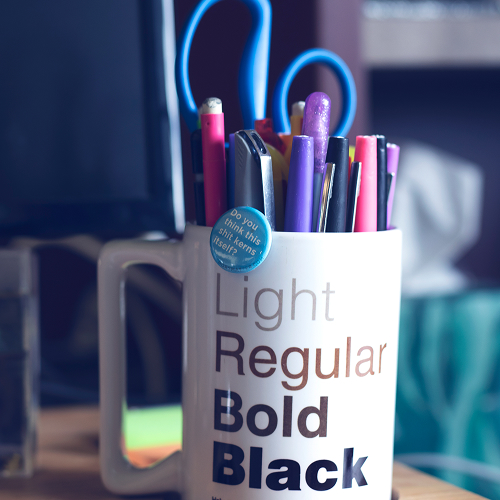 Cup of pens with a pin that says Do you think this shit kerns itself.