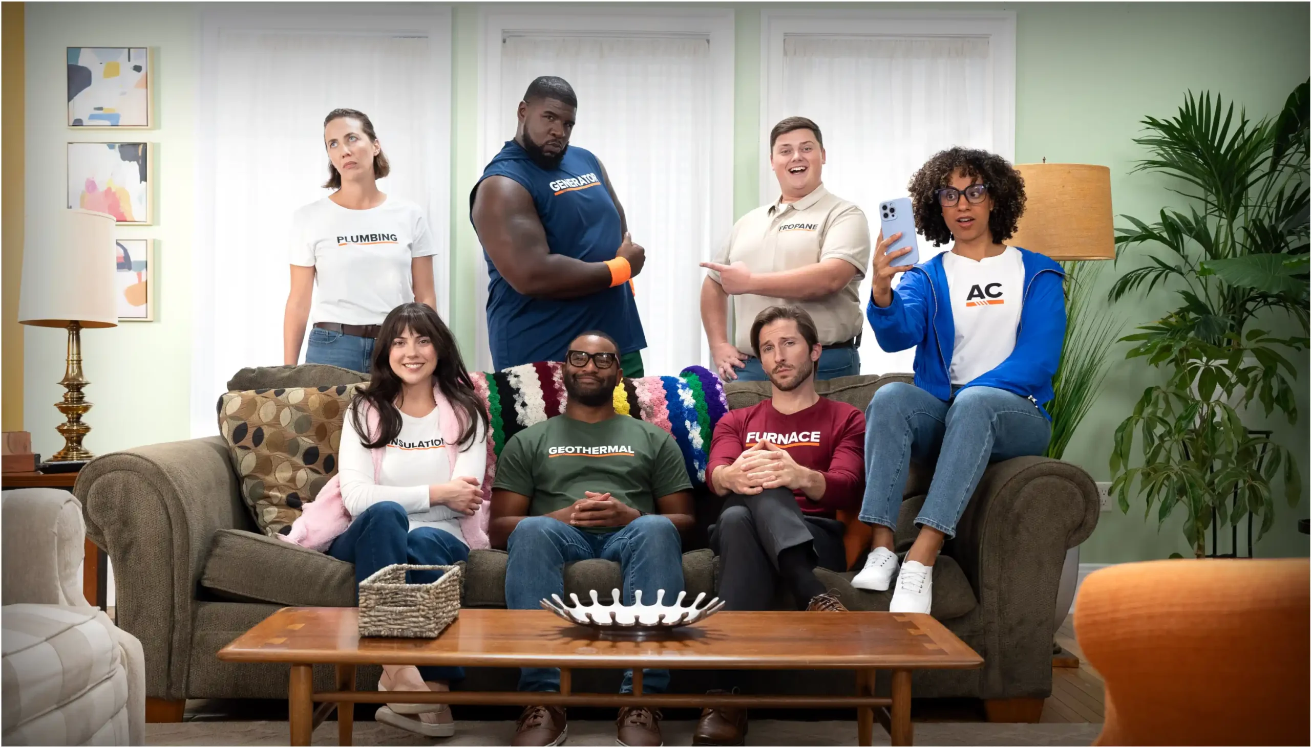 Group of characters wearing shirts that represent different home energy lines of business posing and smiling for a group photo in a living room.