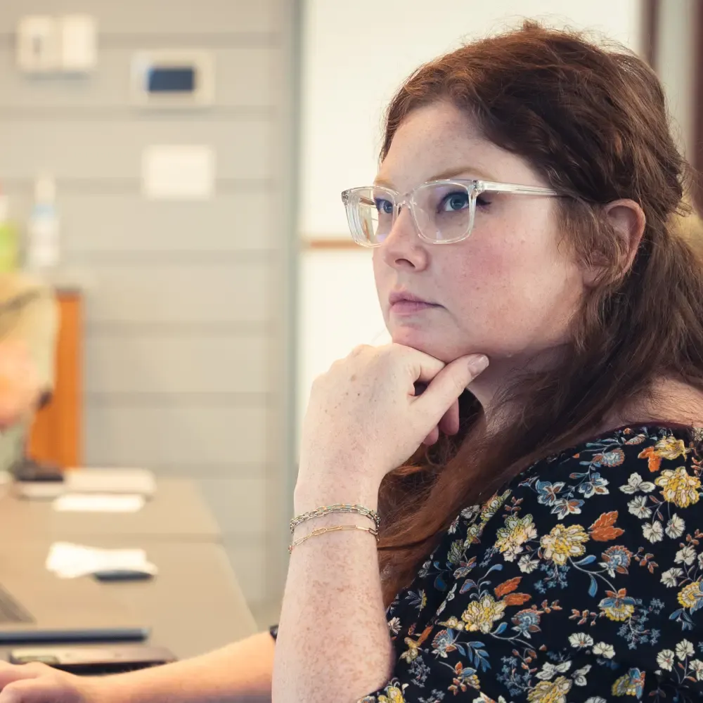 Woman looking pensively up at a screen with her head resting on her hand